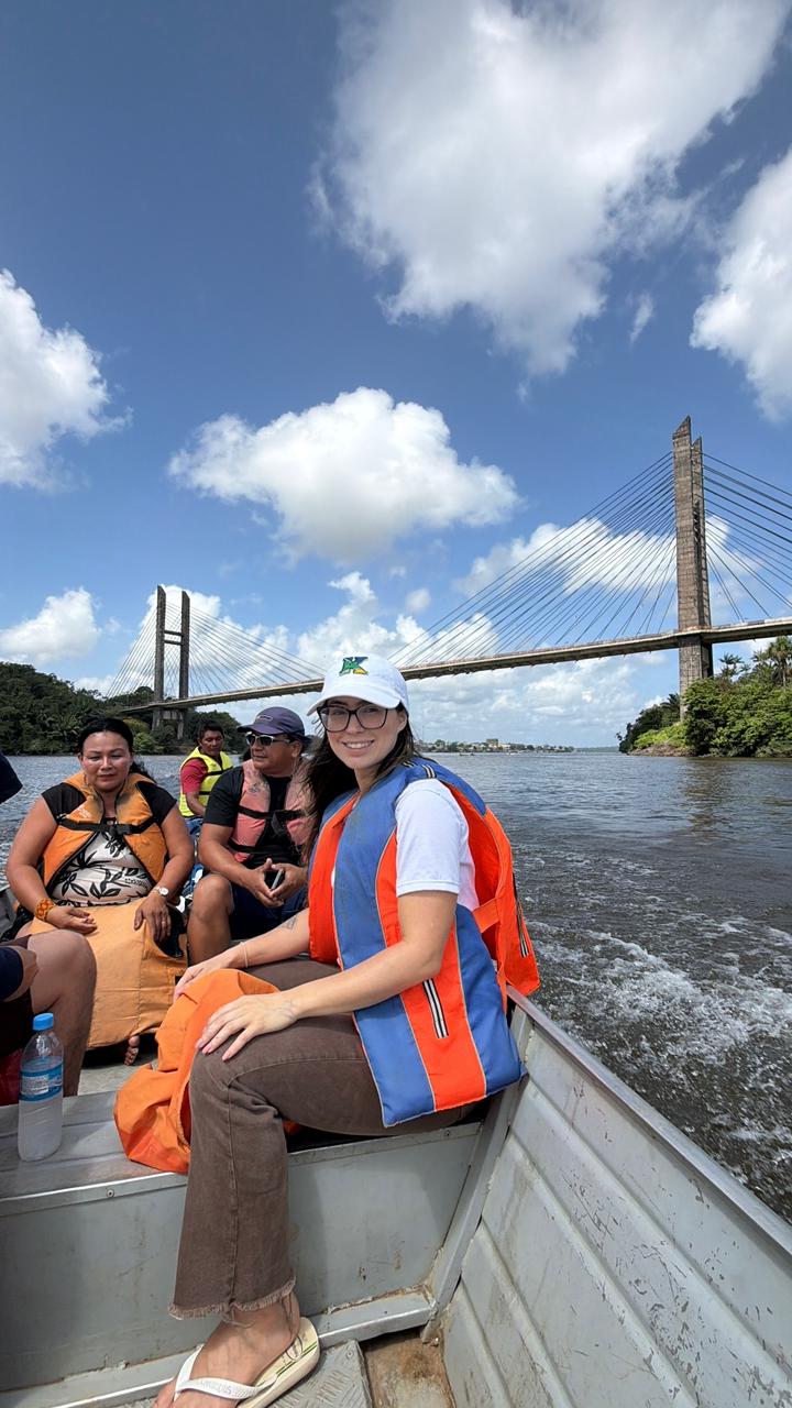 Kamille e outras pessoas em uma embarcação, com uma ponte ao fundo